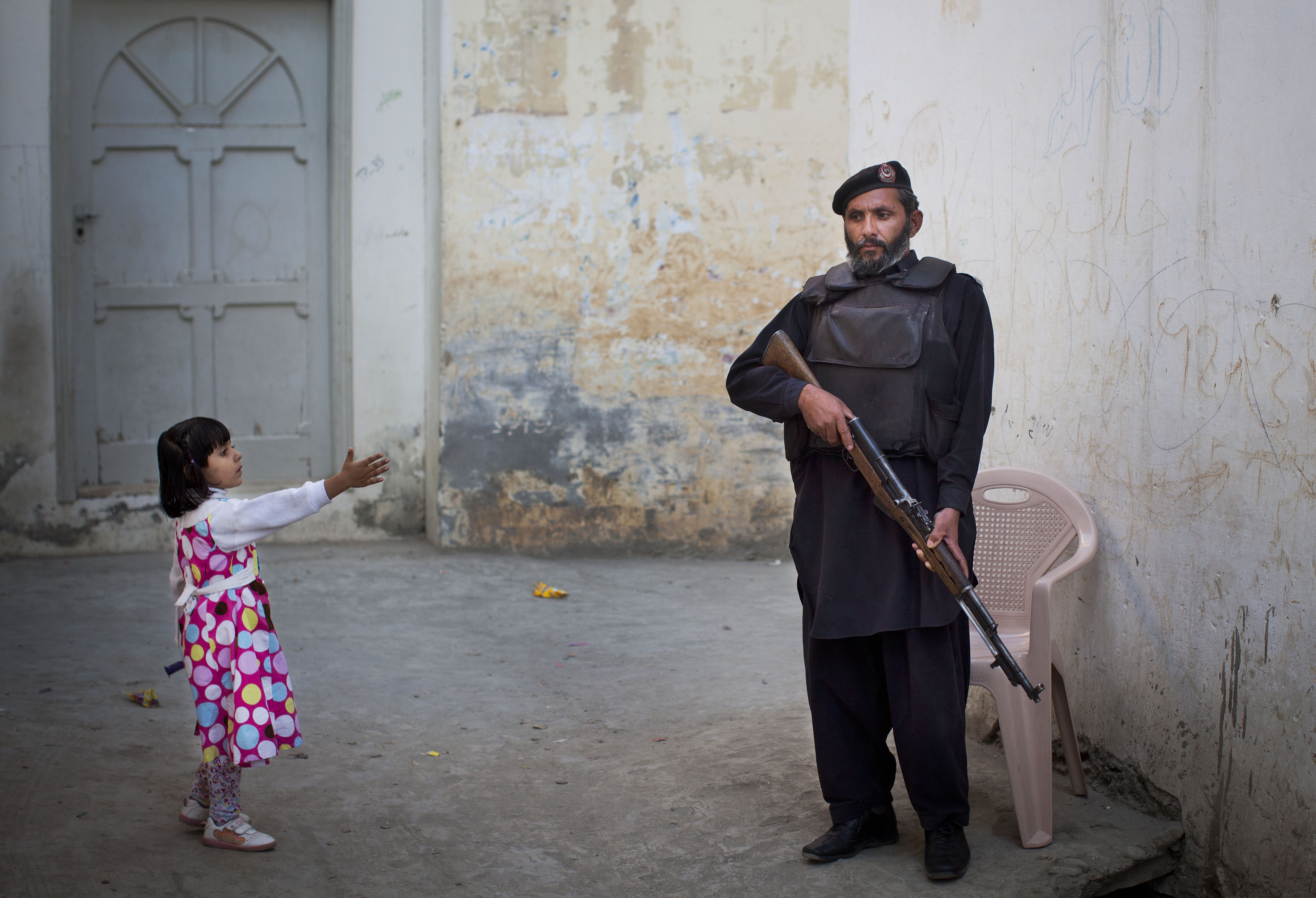 In this Nov. 15, 2012 photo, a young girl reaches out to greet a Pakistani policeman securing the road outside Kainat Riaz's home in Mingora, Swat Valley, Pakistan. Security stepped up after Kainat was wounded by the same Taliban gunman who shot Malala Yousufzai and 13-year-old Shazia Ramazan on Oct. 8 on their way home from school. Malala was shot for her outspoken insistence on girls' education. Shazia and Kainat are to return to school this week for the first time since the shooting. (AP Photo/Anja Niedringhaus)