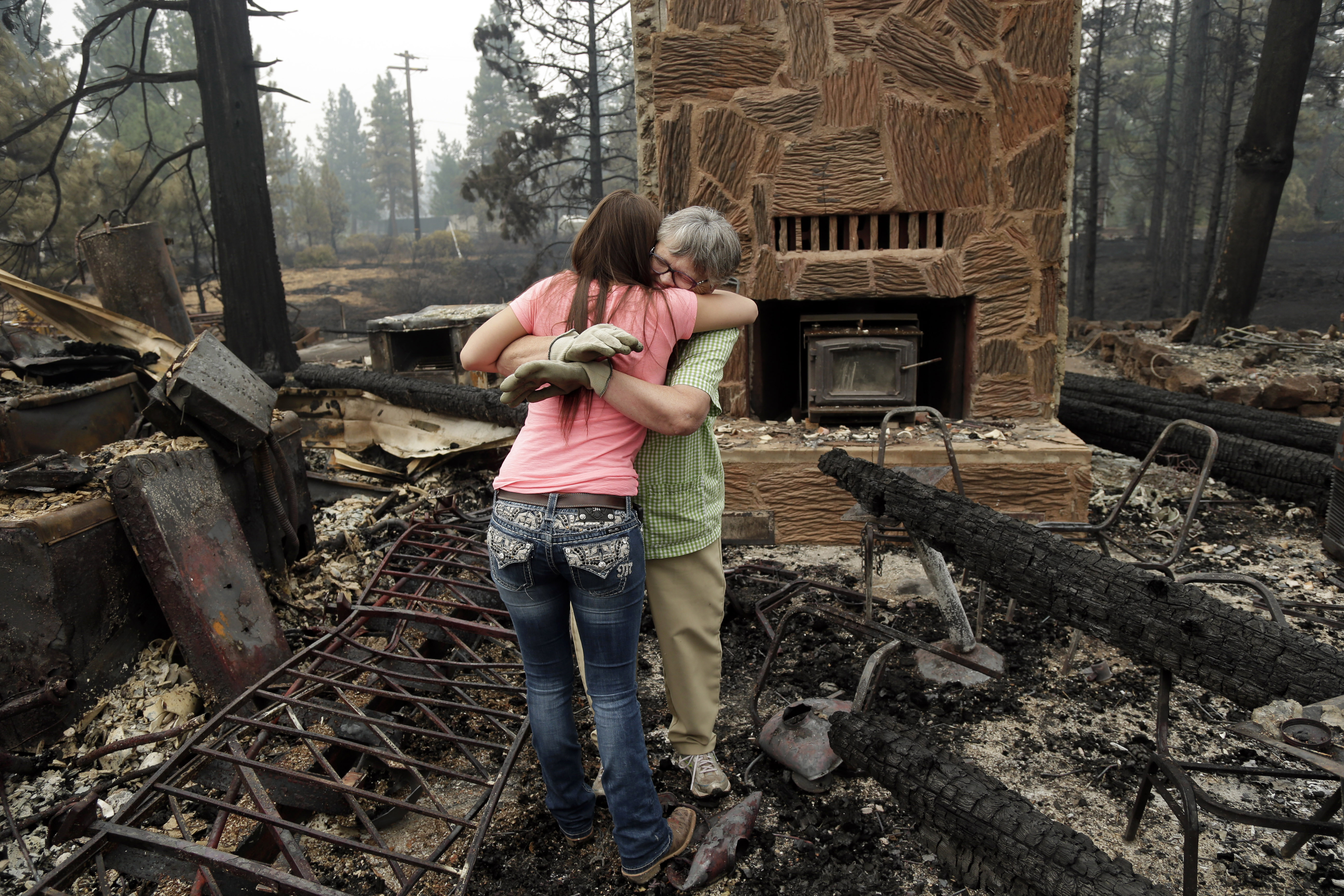 Donna Garner, right, embraces former employee Napua Gonsales-Merck while they shift through the remains of the Fireside Village, a restaurant and shop owned by the Garners for over 30 years, in the aftermath of the Eiler Fire on Tuesday, Aug. 5, 2014, in Hat Creek, Calif. Light rain and higher humidity are helping crews make progress in their fight against two wildfires in the Northern California forest that are just miles apart. (AP Photo/Marcio Jose Sanchez)