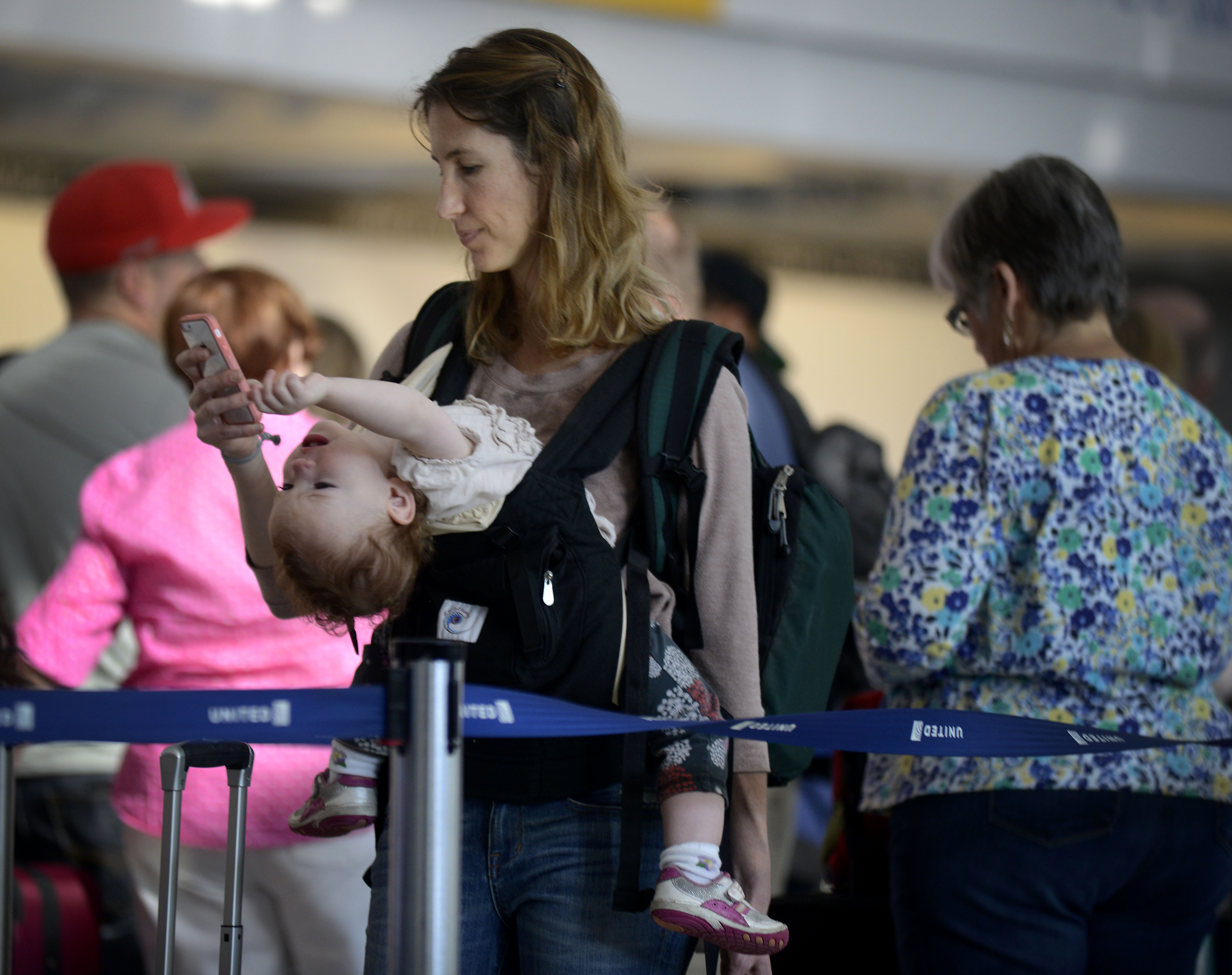 Ann Walden checks her phone as 15 month-old daughter Delphine plays while waiting in-line after their flight to Baton Rouge was delayed at O'Hare International Airport in Chicago, Friday, Sept. 26, 2014. All flights in and out of Chicago's two airports were halted Friday after a fire at a suburban air traffic control facility sent delays and cancellations rippling through the U.S. air travel network. Authorities said the blaze was intentionally set by a contract employee of the Federal Aviation Administration and had no ties to terrorism.   (AP Photo/Paul Beaty)