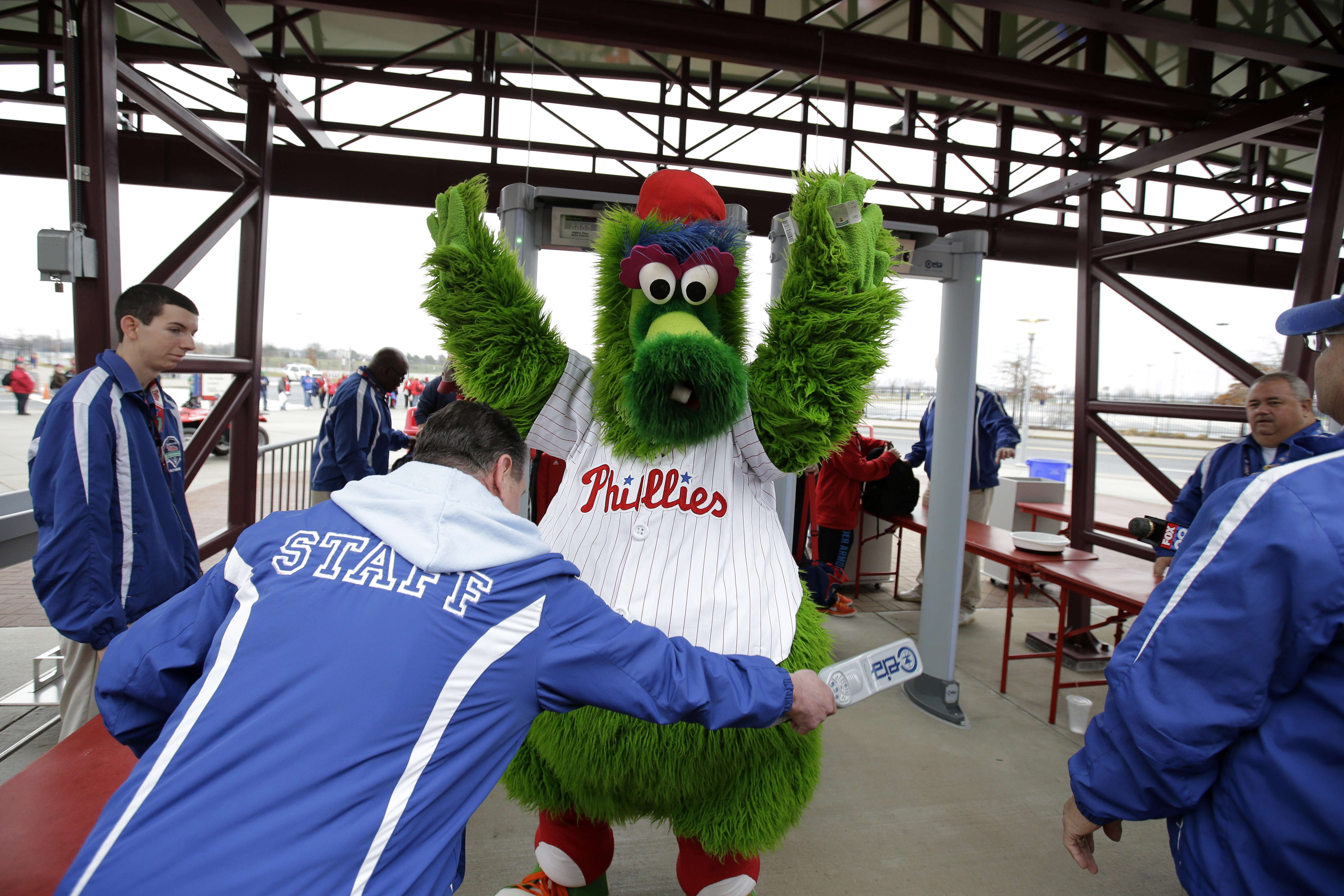 The Philadelphia Phillies' mascot, the Phillie Phanatic, is screened by security personnel for the media before an exhibition baseball game against the Pittsburgh Pirates, Friday, April 3, 2015, in Philadelphia. Citizens Bank Park has installed walk-through metal detectors to comply with Major League Baseball's new rule that all spectators be scanned before entering its stadiums. (AP Photo/Matt Slocum)