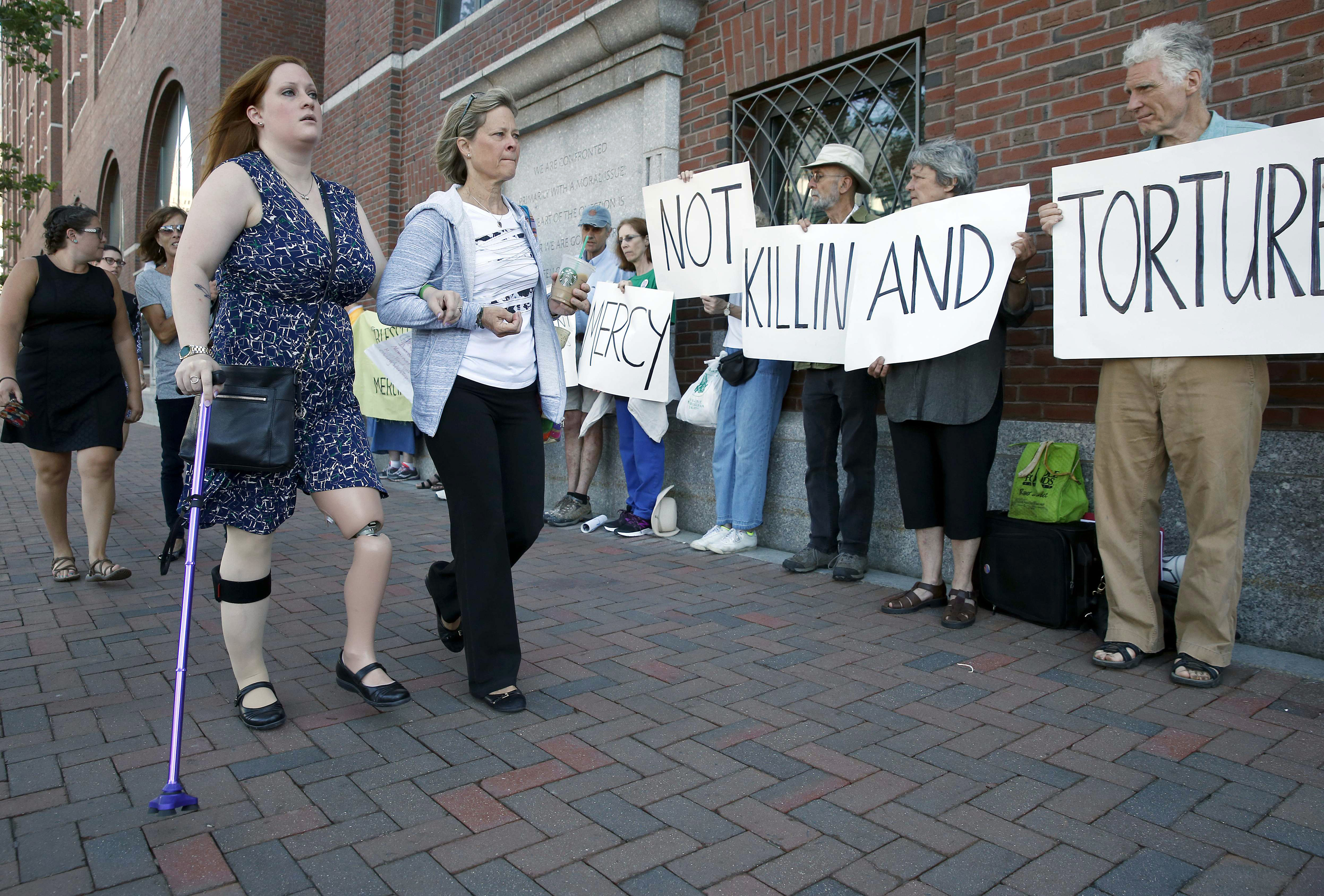Boston Marathon bombing victim Erika Brannock, foreground left, and her mother Carol Downing, foreground right, walk past demonstrators outside federal court in Boston, Wednesday, June 24, 2015. More than 20 victims of the Boston Marathon bombing and their family members are expected to address the court regarding the attack's impact on their lives before a judge formally sentences bomber Dzhokhar Tsarnaev to death. (AP Photo/Michael Dwyer)