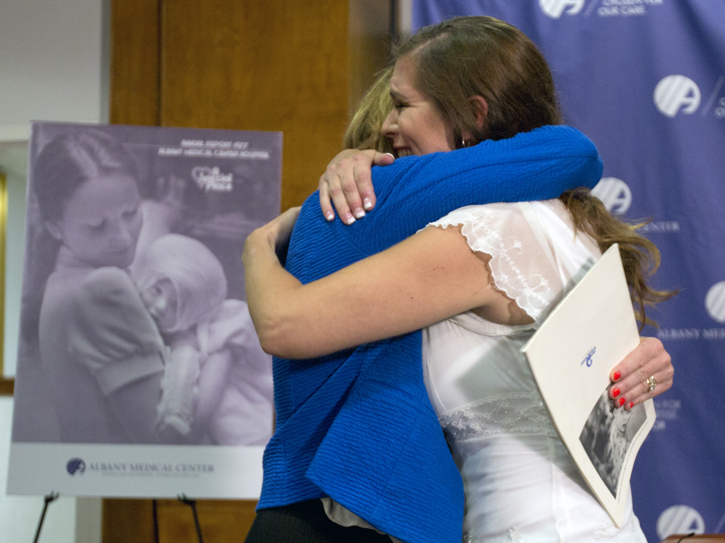 Nurse Susan Berger, left, and Amanda Scarpinati hug during a news conference at Albany Medical Center, Tuesday, Sept. 29, 2015, in Albany, N.Y. Scarpinati, who suffered severe burns as an infant, is finally getting the chance to thank Berger who cared for her, thanks to a social media posting that revealed the identity of the nurse in 38-year-old photos. (AP Photo/Mike Groll)