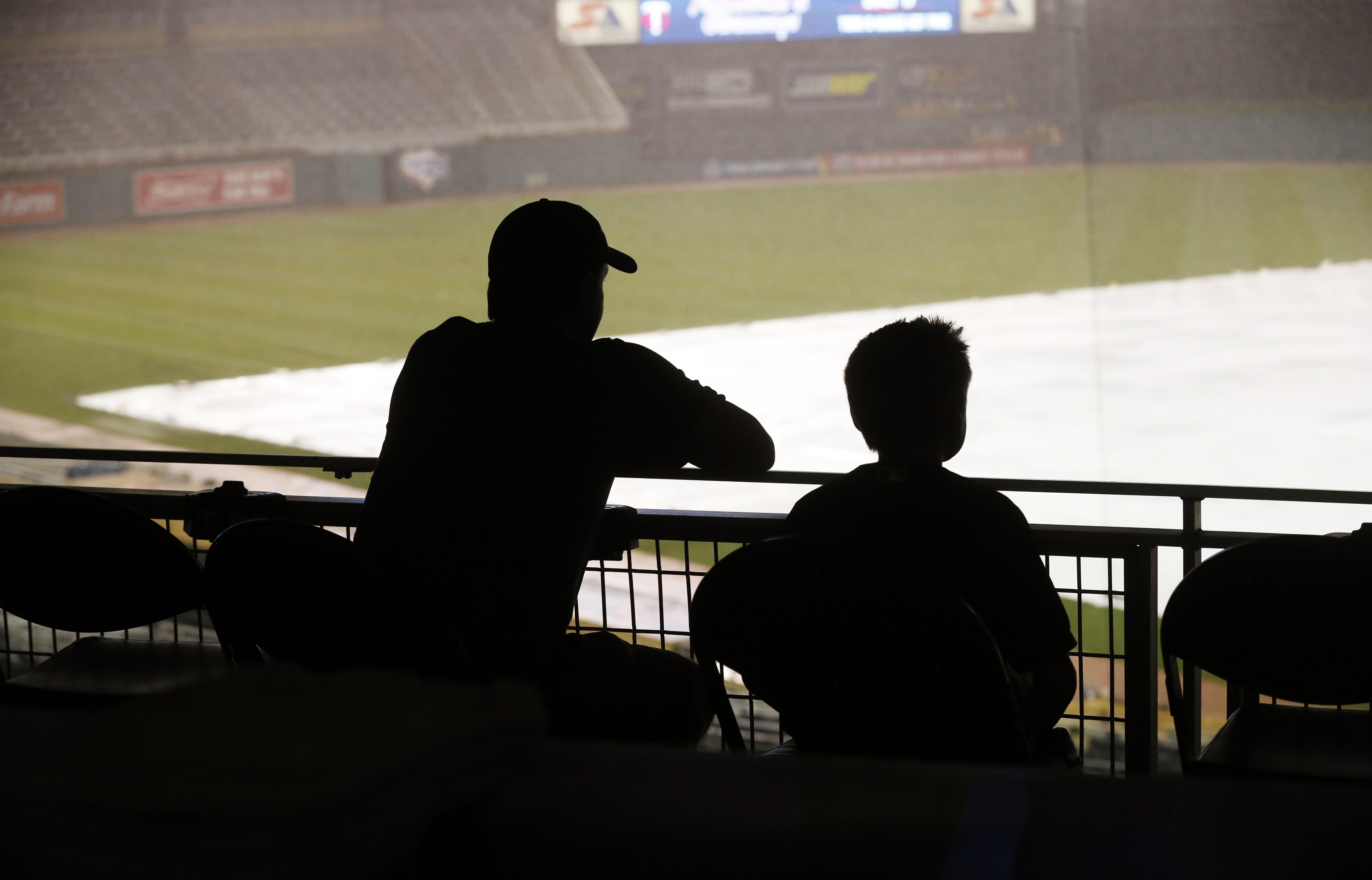 A man and boy look out to the tarp-covered infield at Target Field where heavy rain, lightning and wind delayed the start of the baseball game between the Minnesota Twins and the Oakland Athletics on Tuesday, July 5, 2016. (AP Photo/Jim Mone)