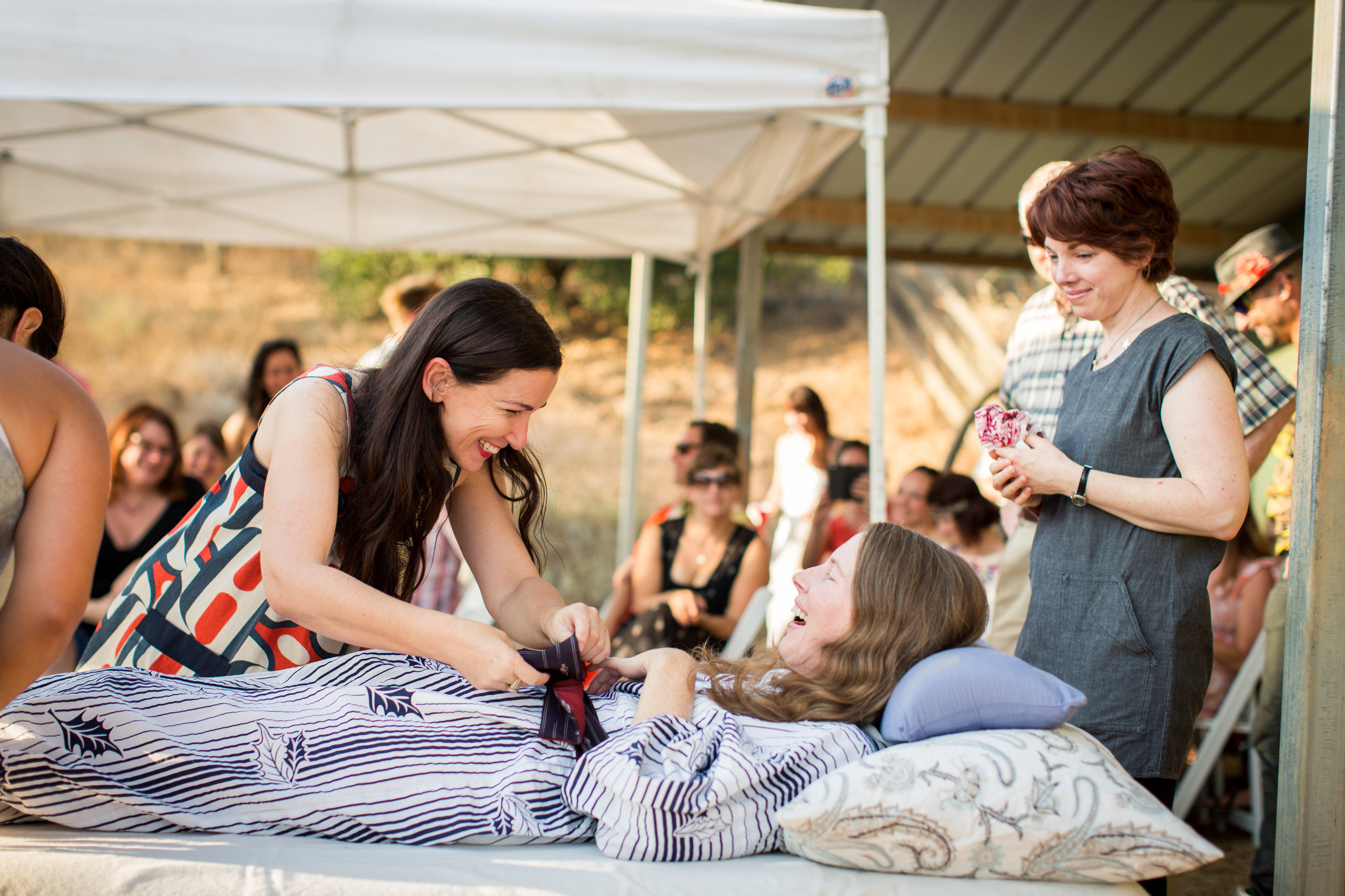 This July 24, 2016 photo provided by Niels Alpert, Amanda Friedland, left, surrounded by friends and family adjusts her friend Betsy Davis's sash as she lays on a bed during her "Right To Die Party" in Ojai, Calif. In early July, Davis emailed her closest friends and family to invite them to a two-day celebration, telling them: "These circumstances are unlike any party you have attended before, requiring emotional stamina, centeredness, and openness. And one rule: No crying." The 41-year-old woman diagnosed with ALS,  held the party to say goodbye before becoming one of the first California residents to take life-ending drugs under a new law that gave such an option to the terminally ill. (Niels Alpert via AP)