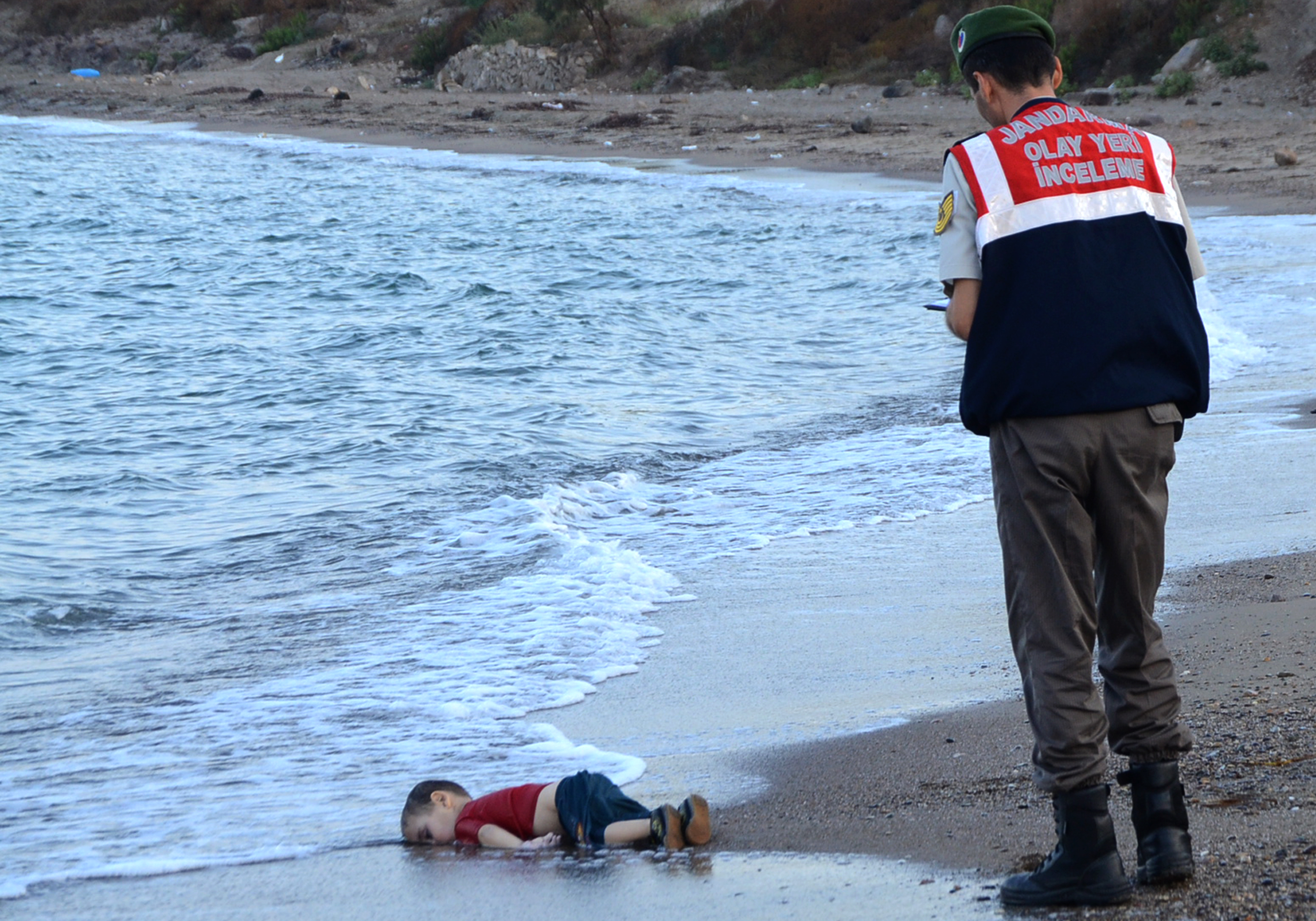 A Turkish police officer stands next to a migrant child's dead body  off the shores in Bodrum, southern Turkey, on September 2, 2015 after a boat carrying refugees sank while reaching the Greek island of Kos.  Photo: Nilufer Demir/AFP/Getty Images