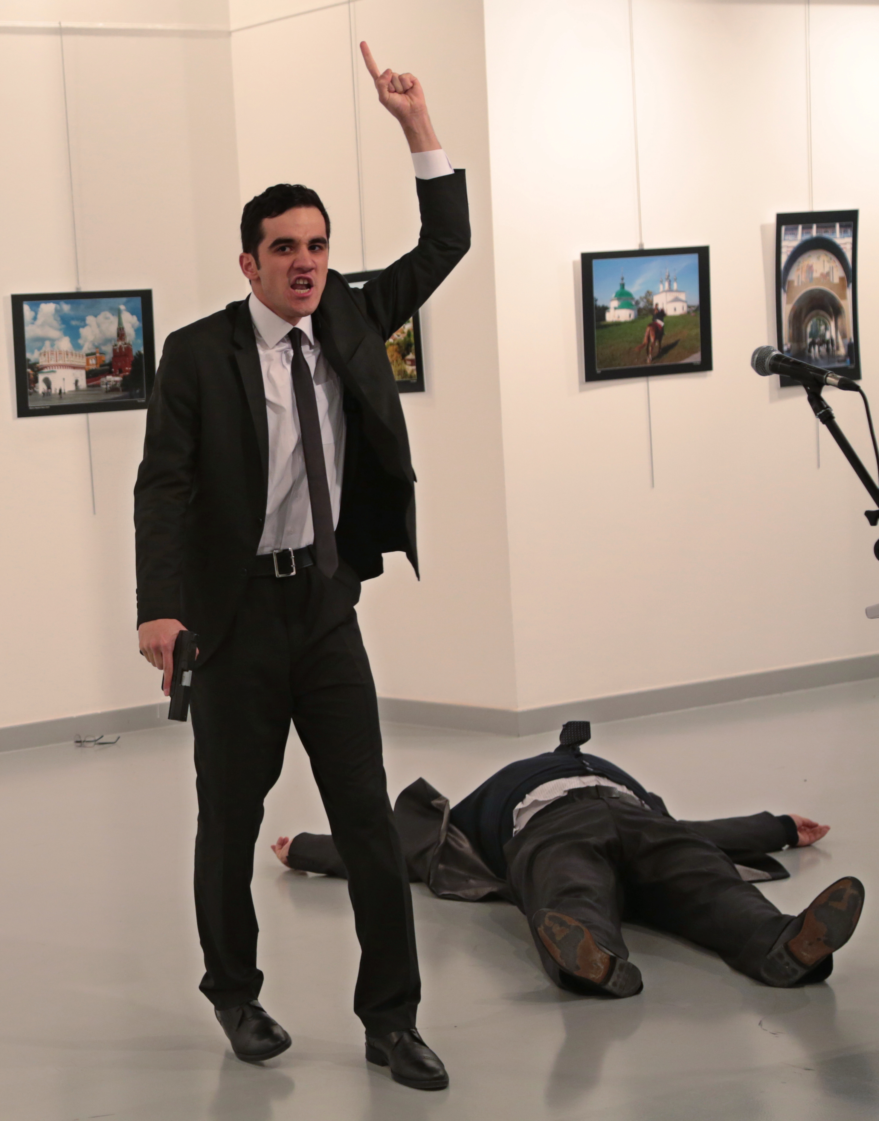 A man gestures after shooting Andrei Karlov, the Russian Ambassador to Turkey, on the floor, at a photo gallery in Ankara, Turkey, Monday, Dec. 19, 2016. The ambassador's condition wasn't immediately known. (AP Photo/Burhan Ozbilici)