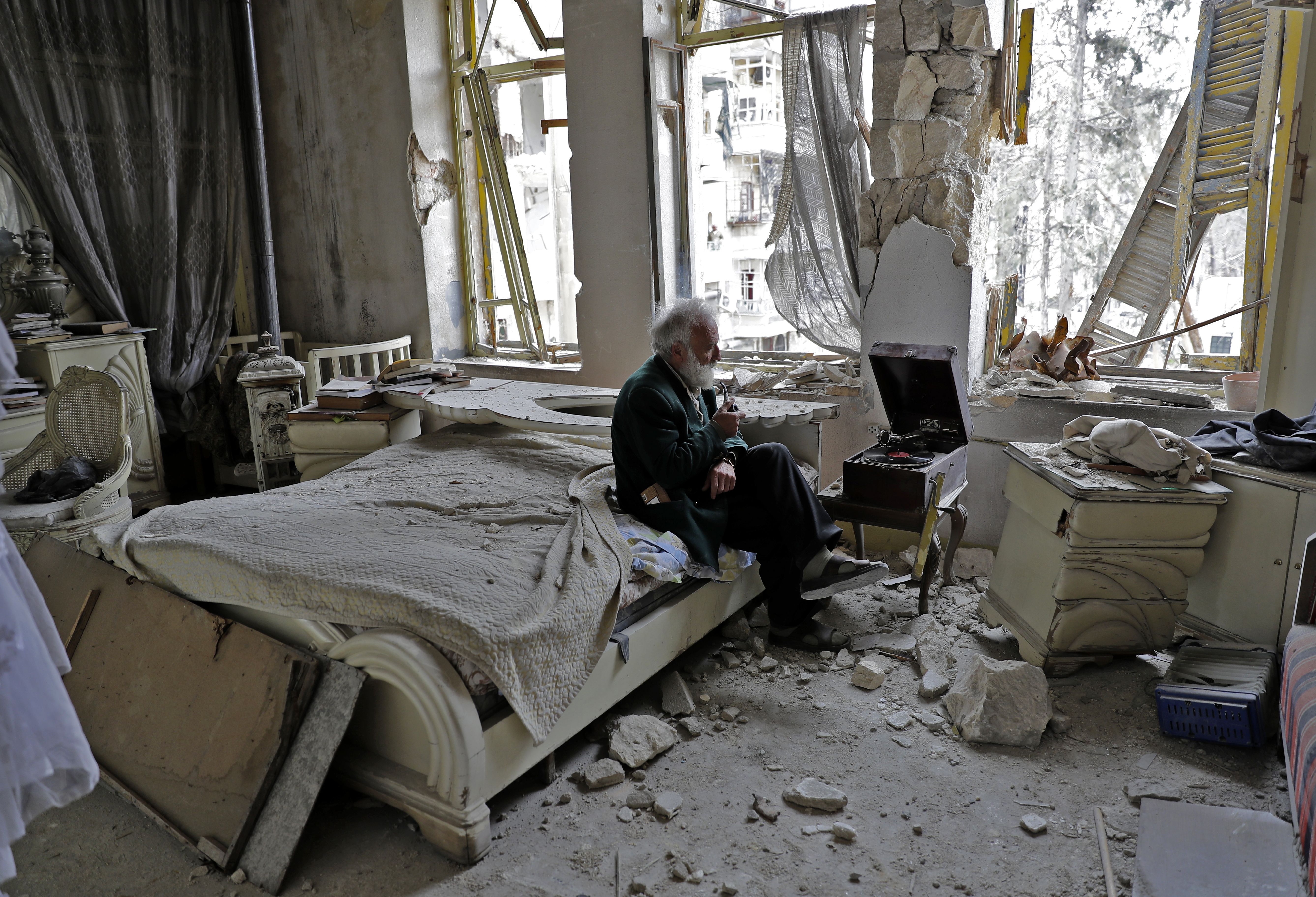  Mohammad Mohiedine Anis, 70, smokes his pipe as he sits in his destroyed bedroom listening to music on his vinyl player, gramophone, in Aleppo's formerly rebel-held al-Shaar neighbourhood. / AFP PHOTO / JOSEPH EID / Getty Images.